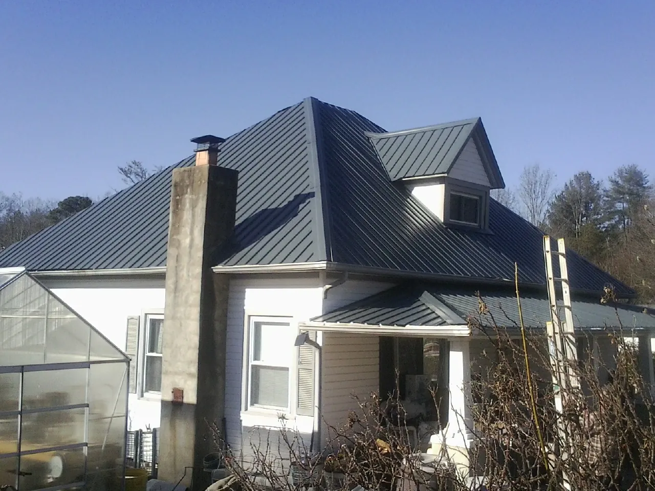 Dark blue standing seam metal roof on a white farmhouse with dormer — Slate & Tile Roof Repair by Roofing Brothers in Grand Meadow