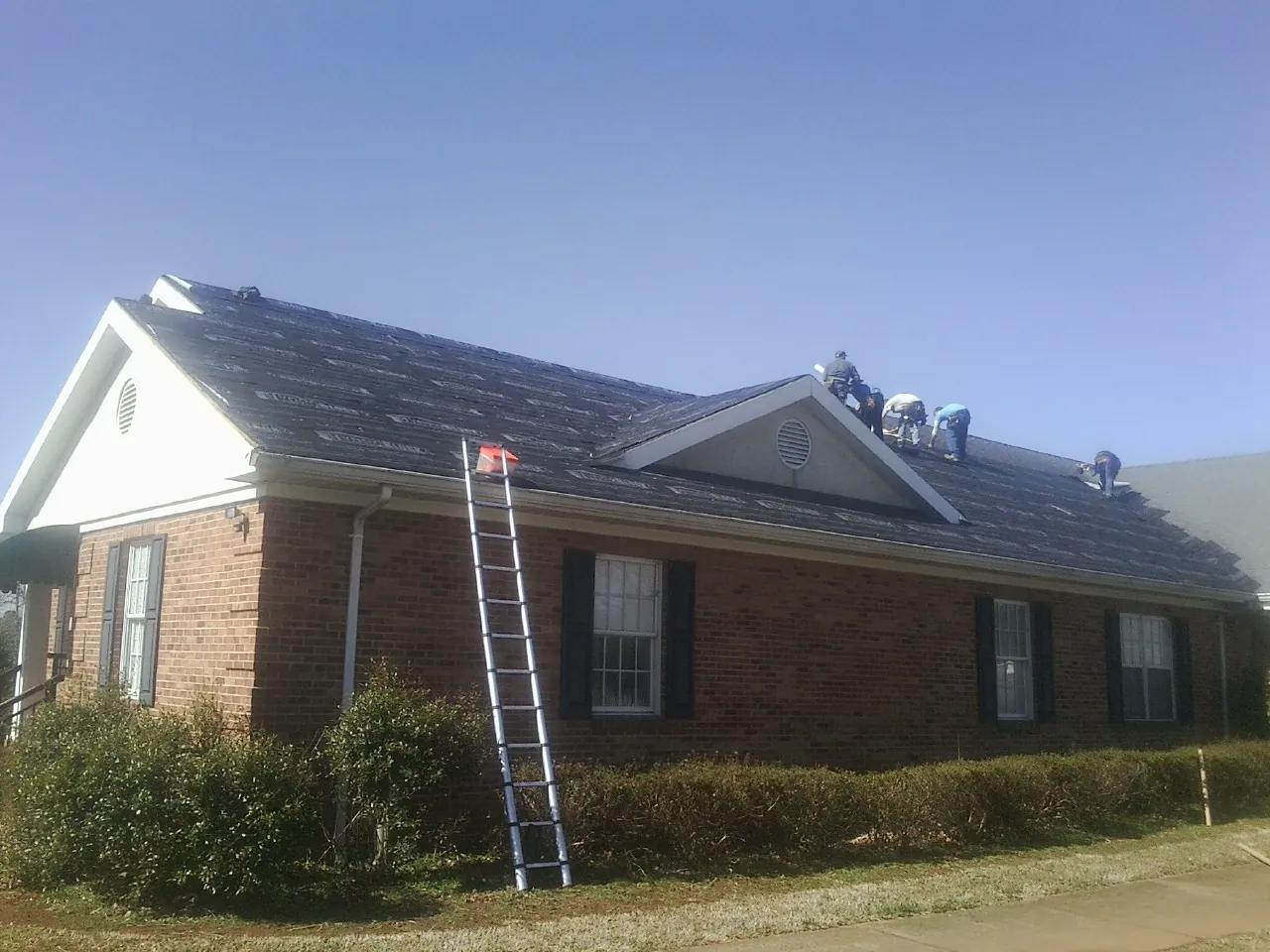 Crew tearing shingles off a brick ranch roof with a ladder set — Metal Roof Repair work by our crew in Grand Meadow