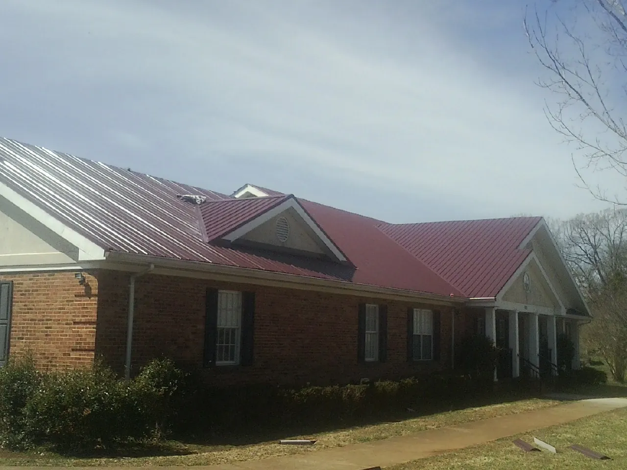 Red metal roof with gabled entries on a long brick building, from a Hail Damage Roof Repair job in Grand Meadow