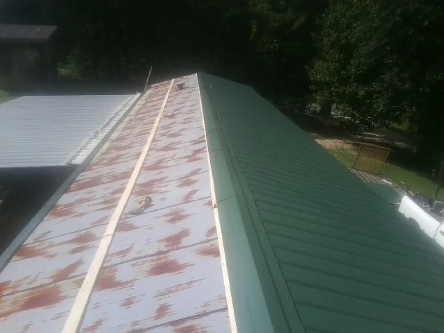Old rusted panels beside newly installed green metal roofing — Wind Damage Roof Repair by Roofing Brothers in Grand Meadow