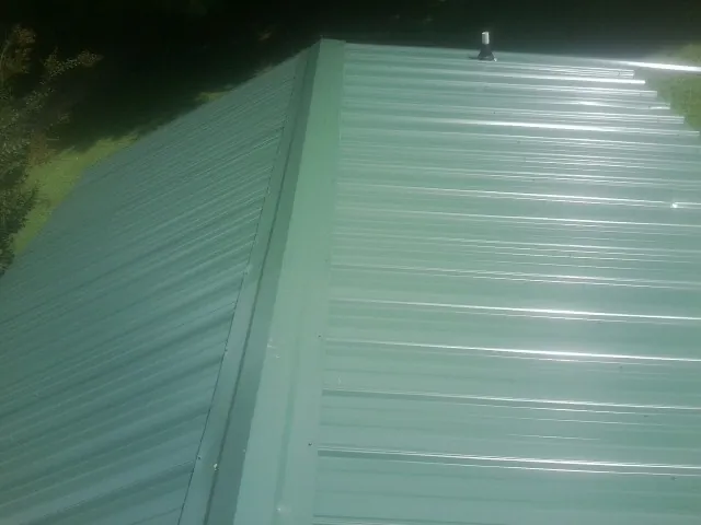 New green metal panels meeting at the ridge of a roof — Flat Roof Repair work by our crew in Grand Meadow