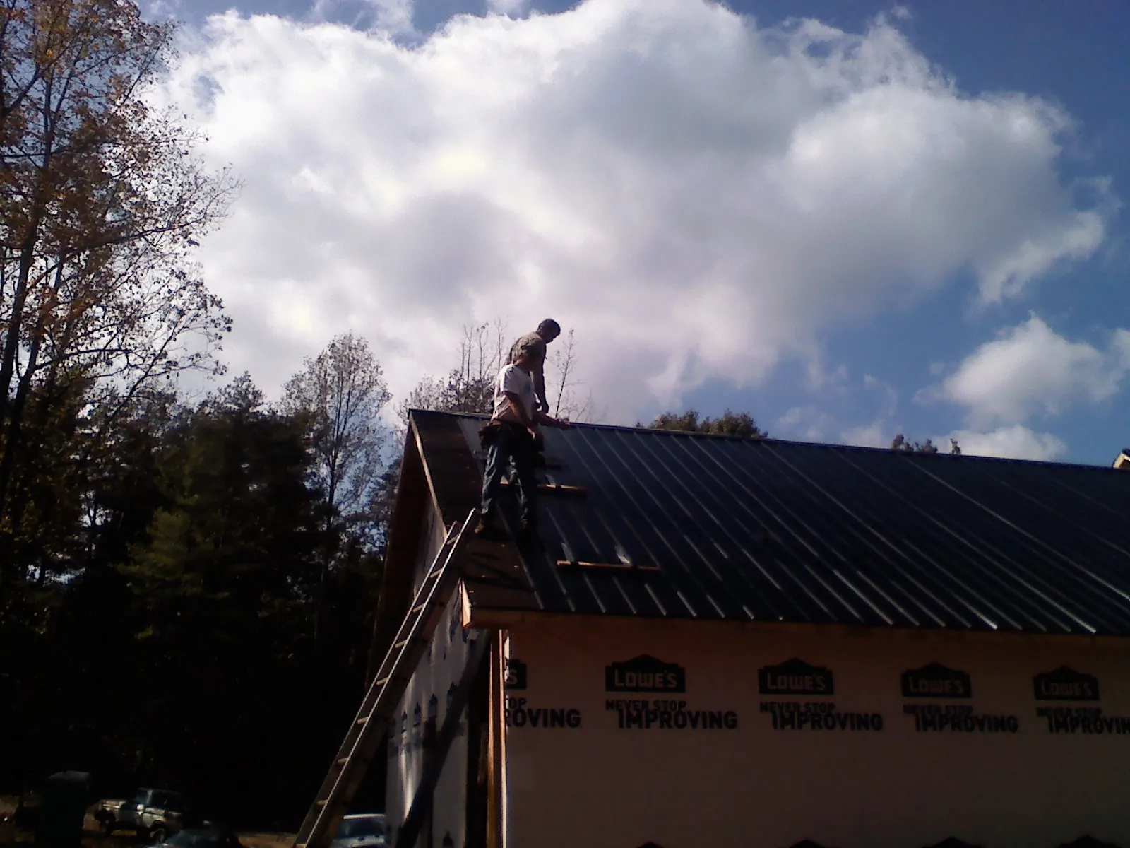Roofer fastening dark metal panels high against a cloudy sky, from a Roof Inspection job in Grand Meadow