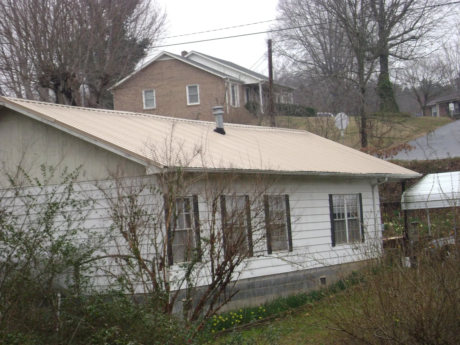 Tan metal roof on a white sided house set into a hillside — Commercial Roofing by Roofing Brothers in Grand Meadow
