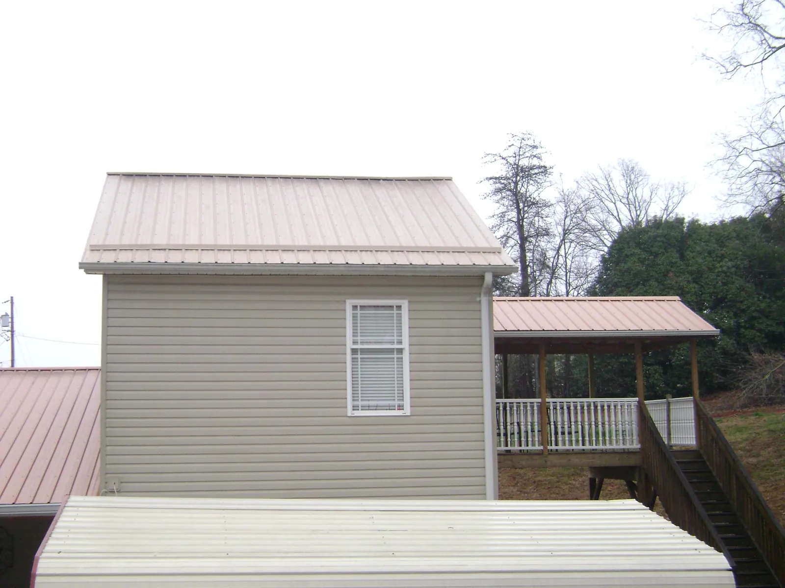 Tan metal roofs on a two story addition and attached porch, from a Roof Replacement job in Grand Meadow